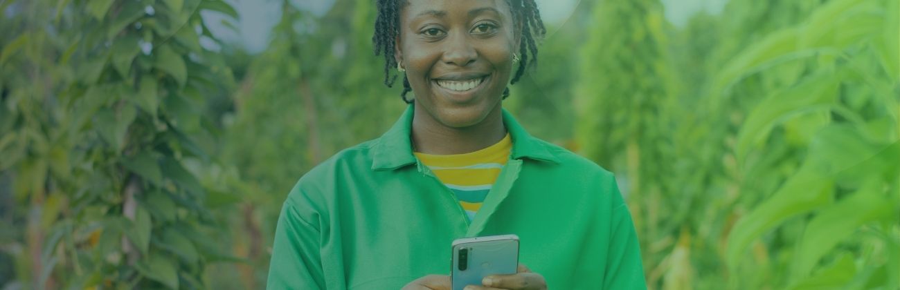 Une femme d'origine africaine tient un smartphone dans ses mains, elle se trouve dans un champ