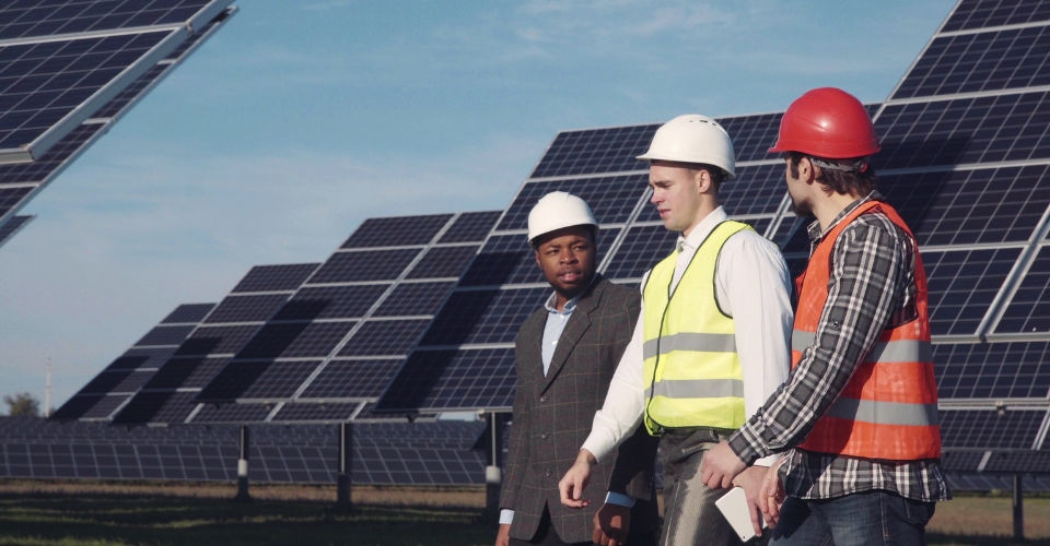 Des hommes en tenue de travail discutent entre eux entourés de panneaux photovoltaïques