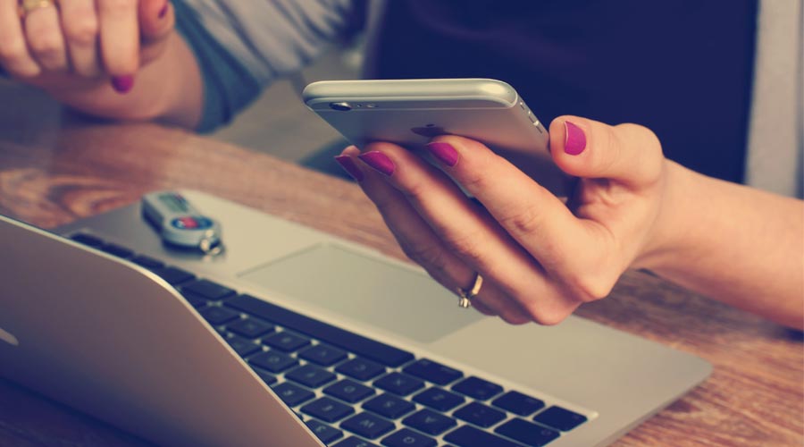 woman at computer with smartphone in hand