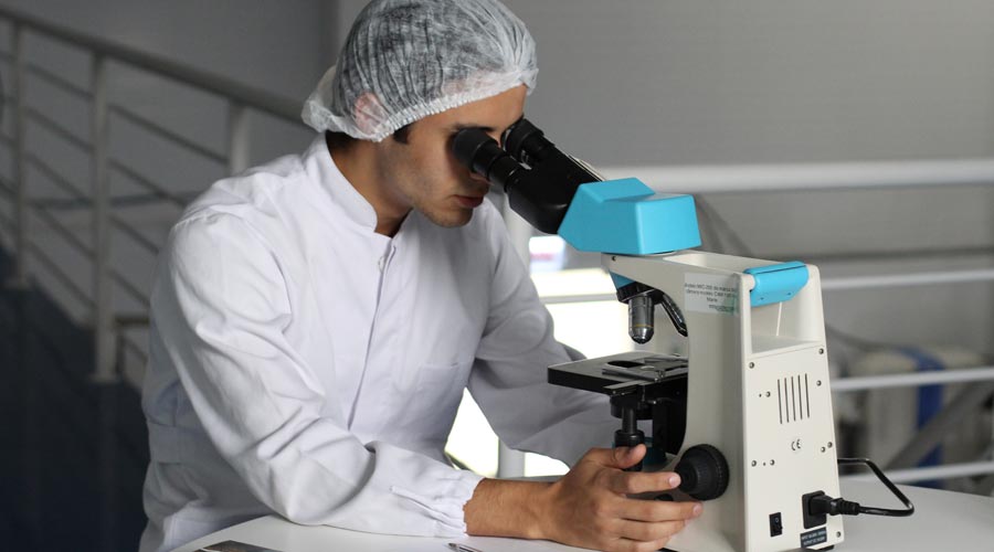 uomo in un laboratorio scientifico che guarda attraverso un microscopio