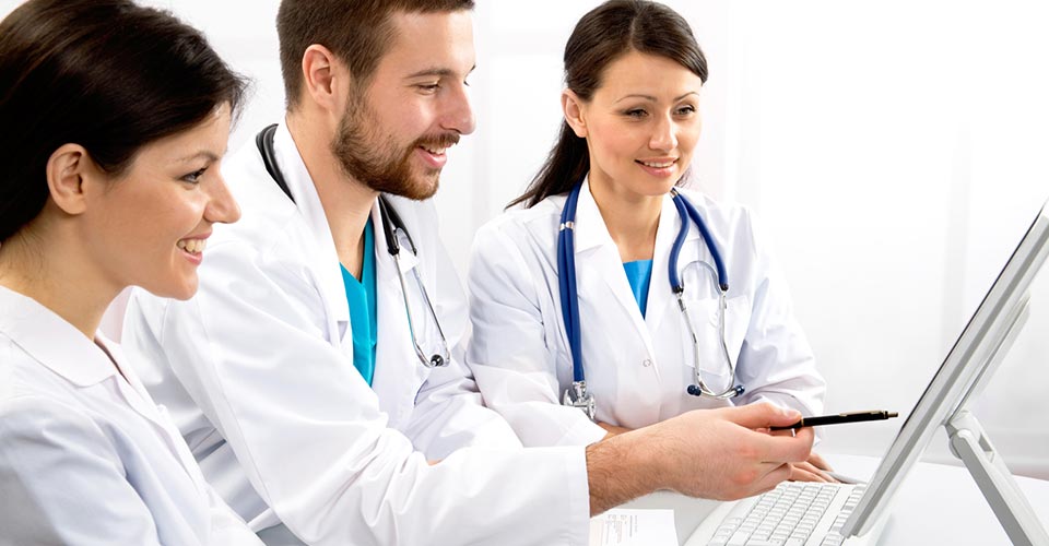 Three carers (two women and one man) in white coats talking in front of a computer screen