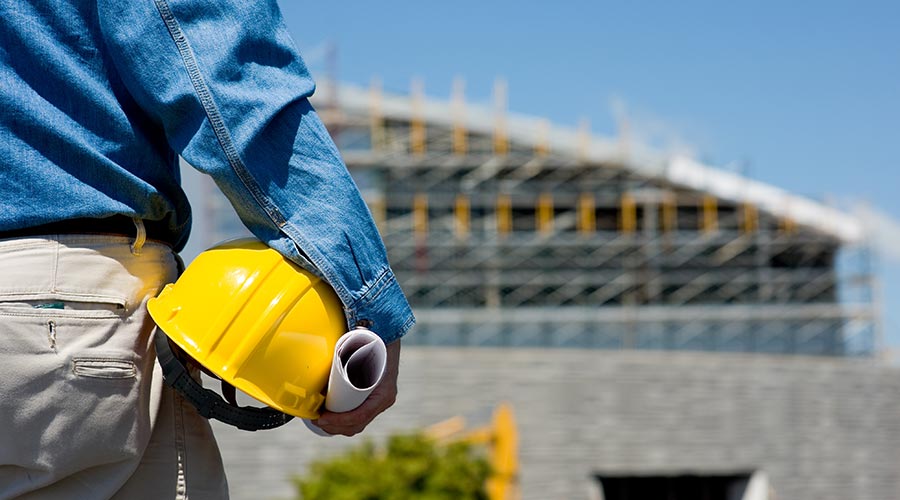 Un homme tient son casque jaune devant un chantier de construction